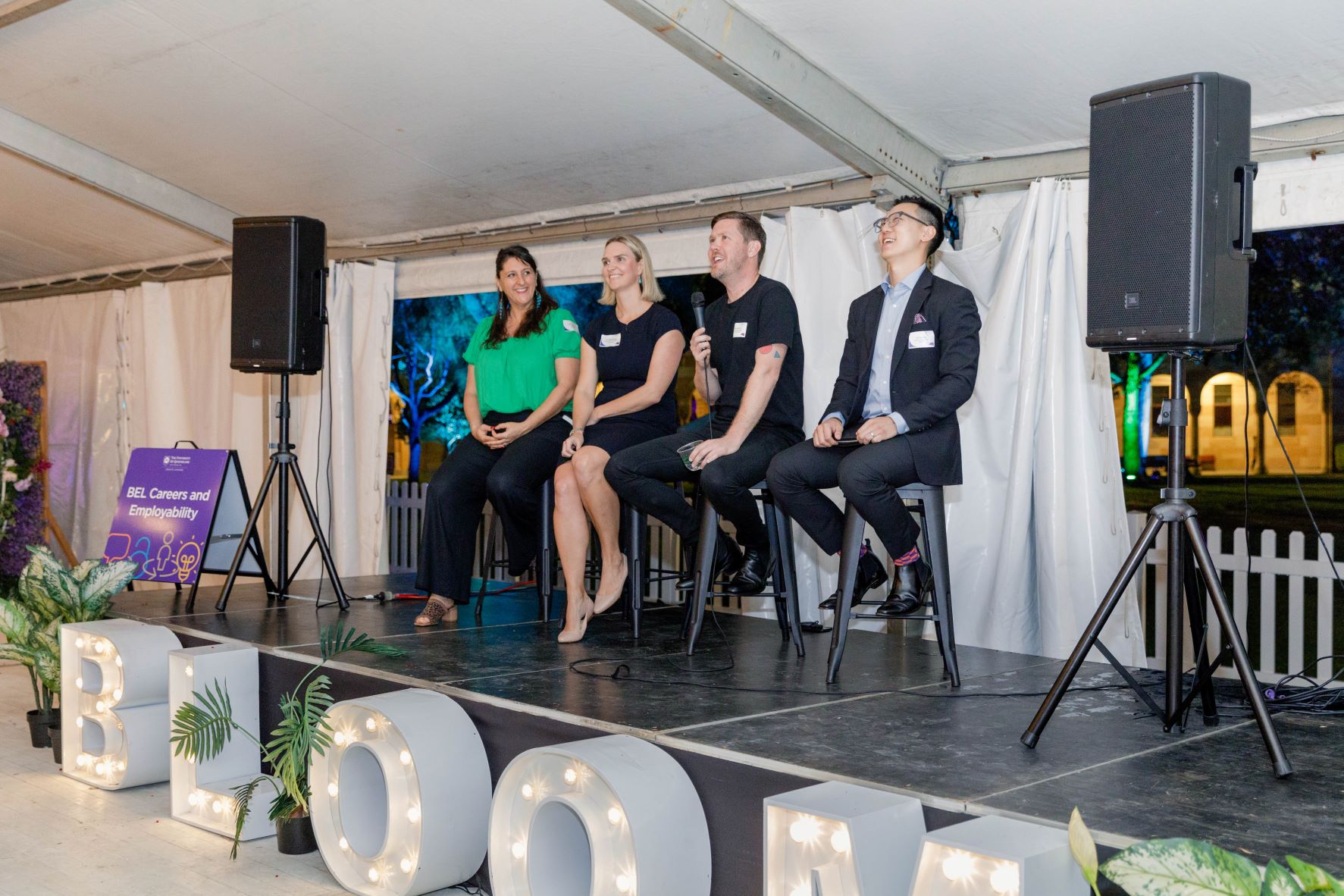 Four people sitting on stools on a stage in front of an audience