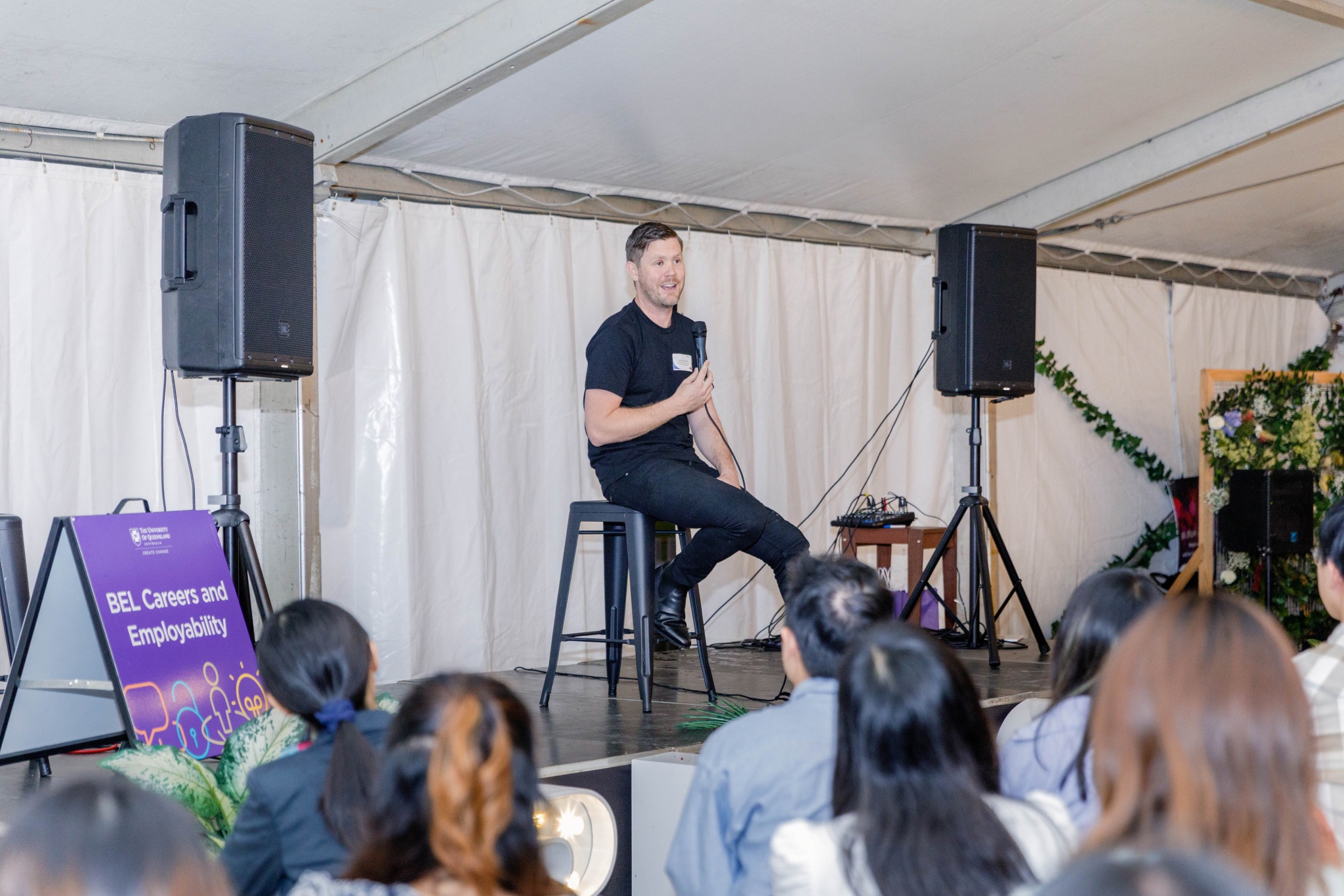 Andy Galloway sitting on a stool in talking to an audience seated in front of him