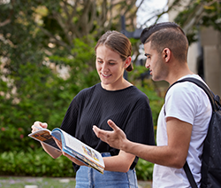 two students with book in front of Colin Clark Building
