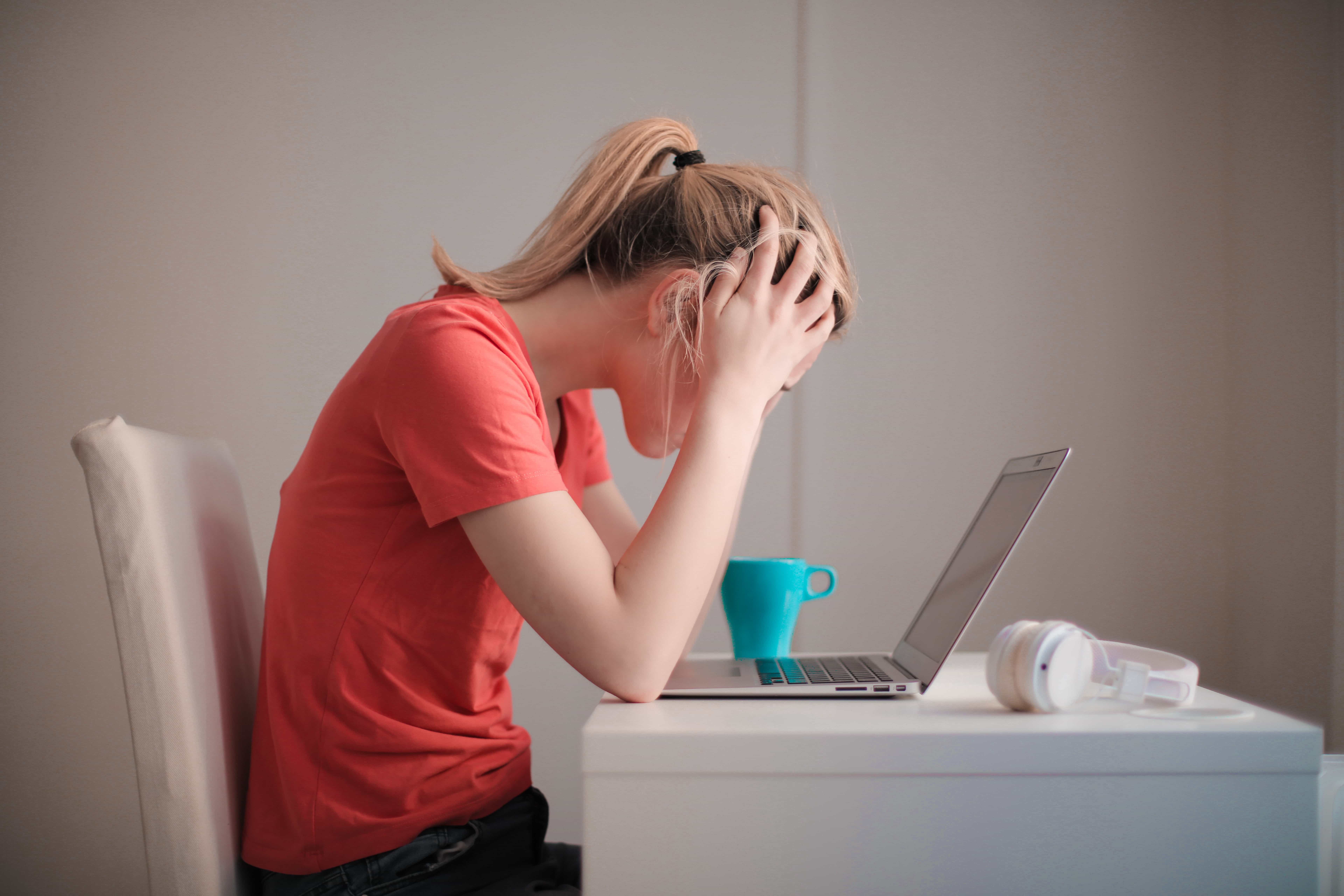 This is an image of a stressed out person sitting at their laptop with their head in their hands