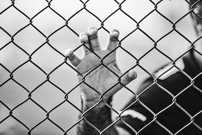 This is a black and white image of a hand gripping a chain link fence