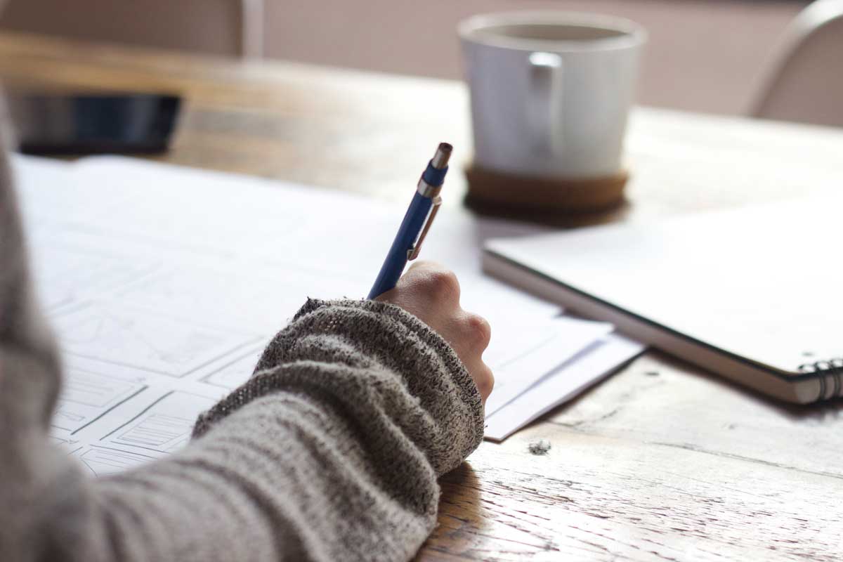 woman's hand, writing in pen with coffee and laptop