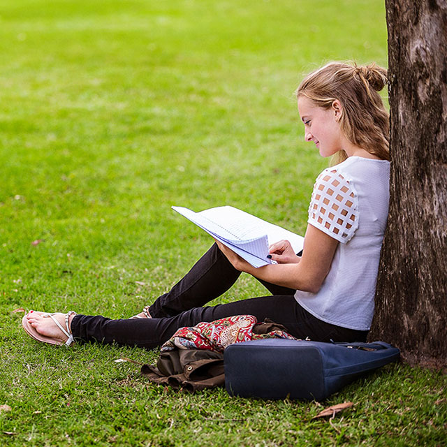 Kate Green sitting reading under a tree at UQ