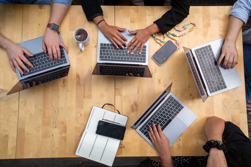 looking down on table of diverse young hands with laptops