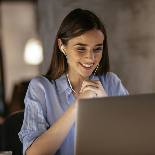 student with ear buds listening, smiling and looking at laptop