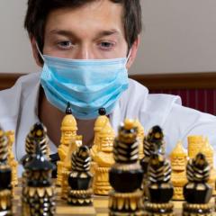 Person wearing a mask looking at a chess board