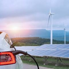 Electric vehicle plugged into a charging station out the front of wind power solar panels 