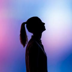silhouetteof a woman staring up with a pink, purple and blue background. 