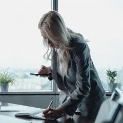 woman in office holding a phone and writing in a notepad